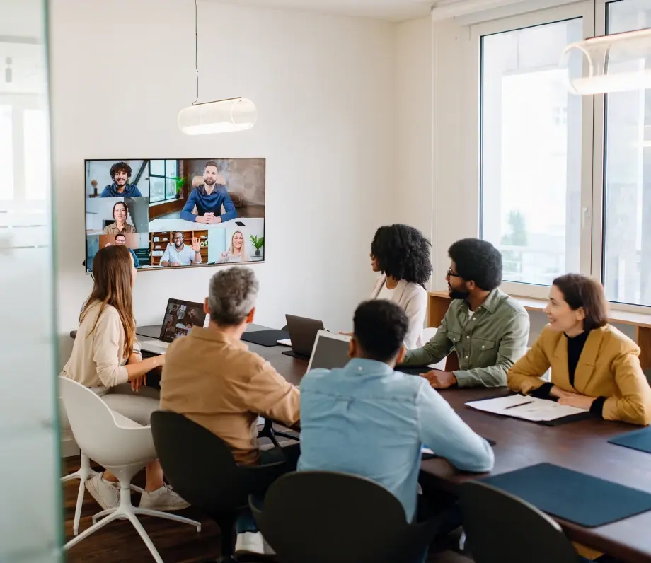 Six people at a meeting table with a further 6 on a TV screen