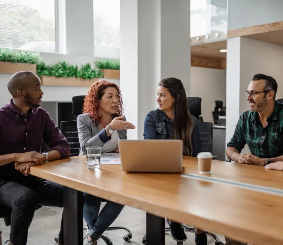Four people around a meeting table with a laptop